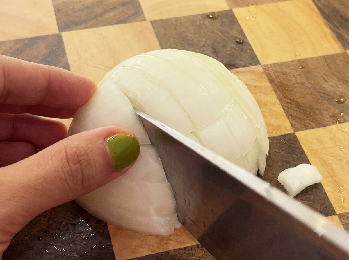 Un cuchillo cortando a través de una cebolla blanca cortada por la mitad en una tabla de cortar de madera a cuadros.