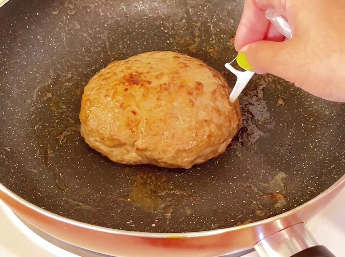 Un palillo insertado en la superficie superior de una hamburguesa gruesa y cocida en una sartén.