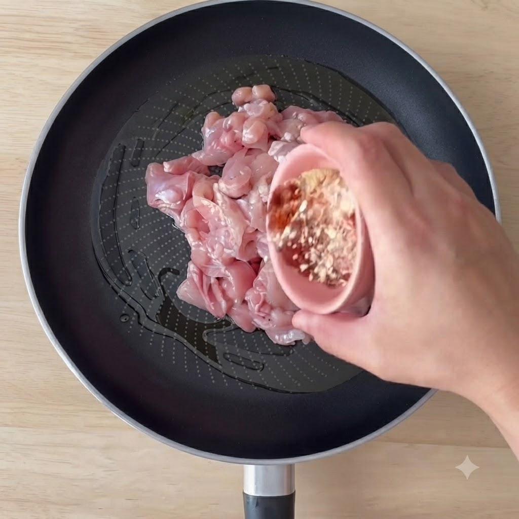Trozos de pollo deshuesado cocinándose en una sartén con aceite de oliva y especias.