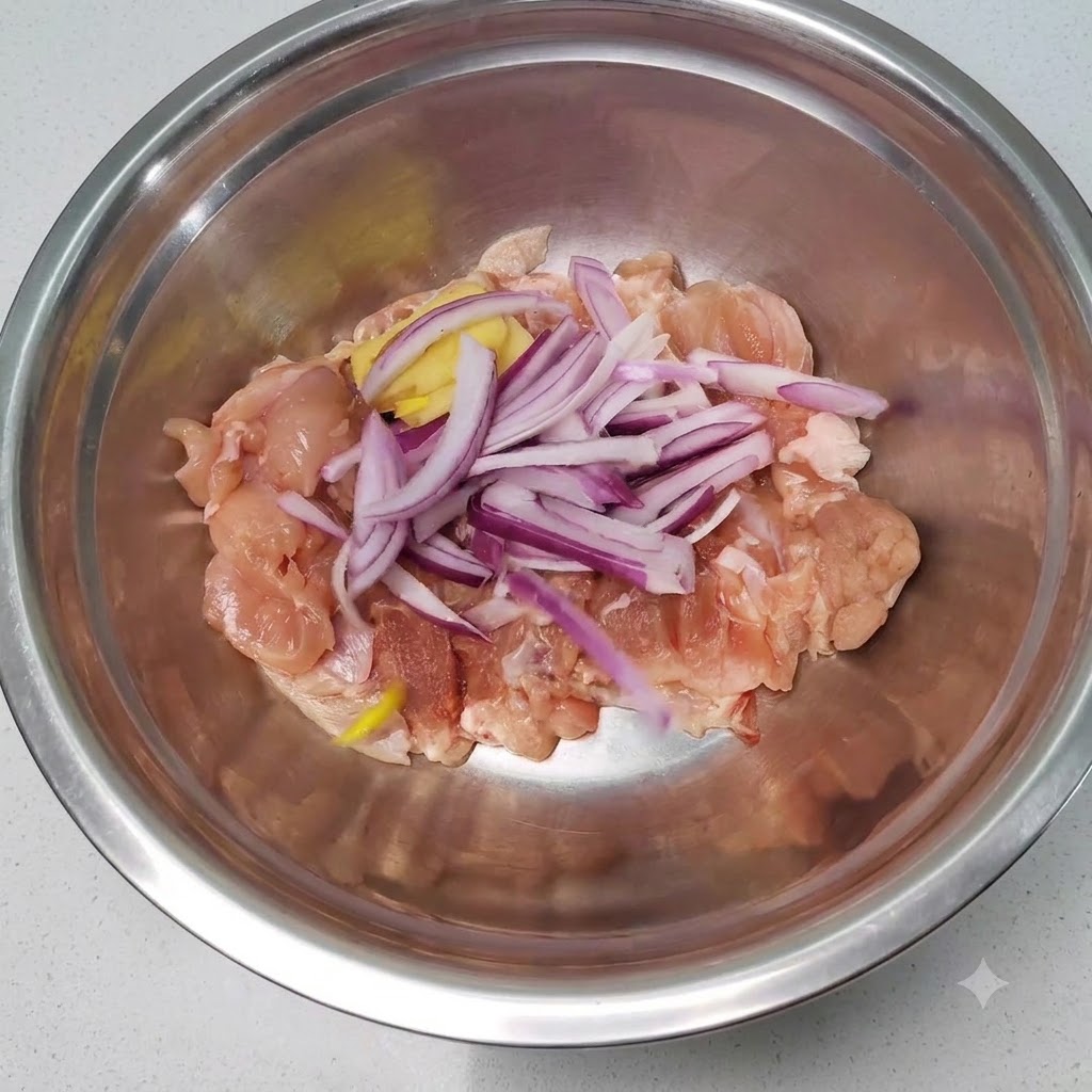 Trozos de pollo crudo mezclados con cebolla en rodajas y jengibre dentro de un bol de mezcla de acero inoxidable.