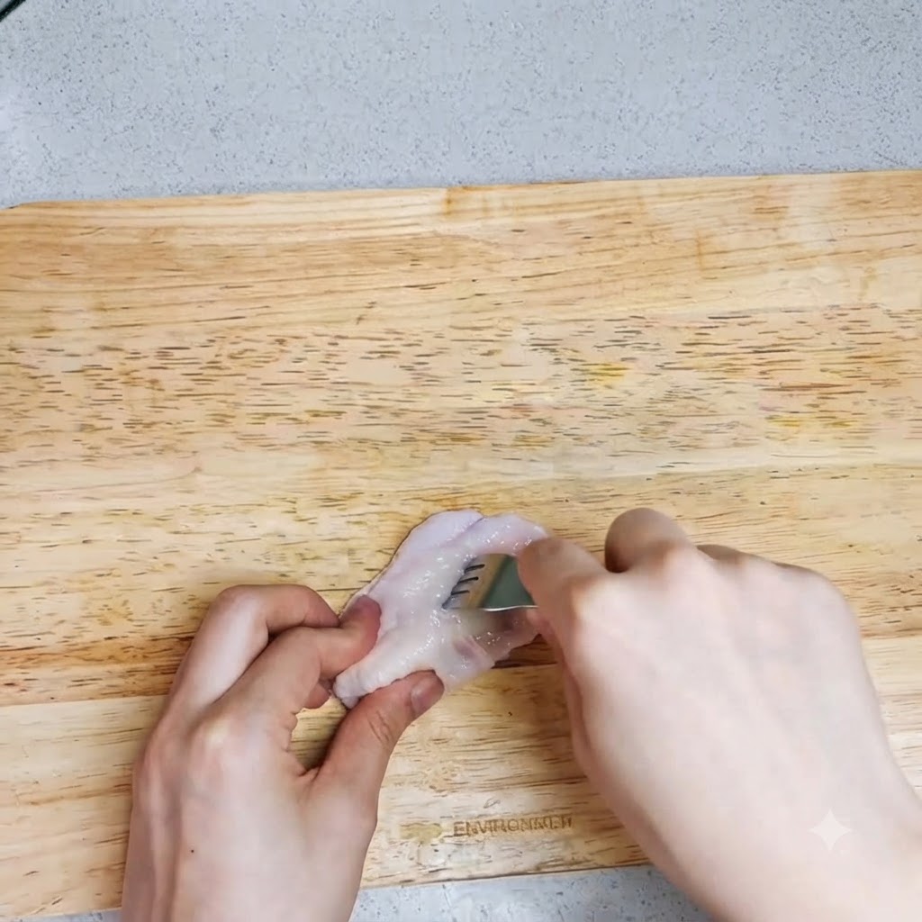 Unas manos usando un tenedor para hacer agujeros en un alita de pollo cruda sobre una tabla de cortar.