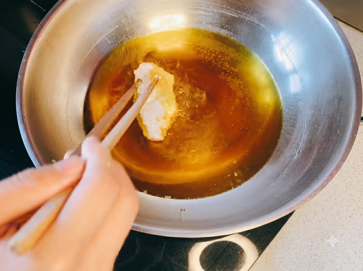 Palillos colocando un trozo de pollo empanizado en una sartén con aceite caliente.