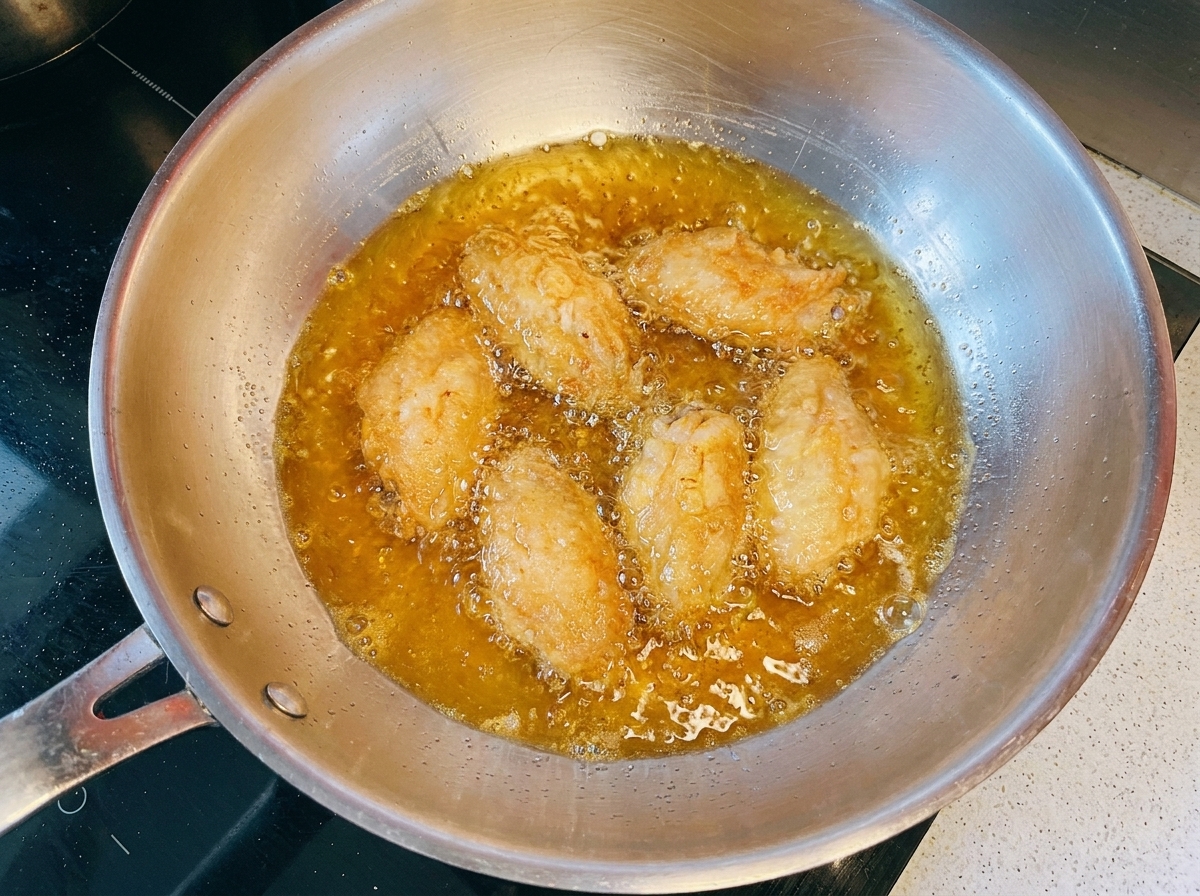 Alitas de pollo dorándose en aceite caliente dentro de una sartén de metal.