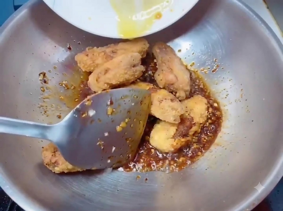 Alitas de pollo fritas extracrujientes transferidas al wok con una espátula.