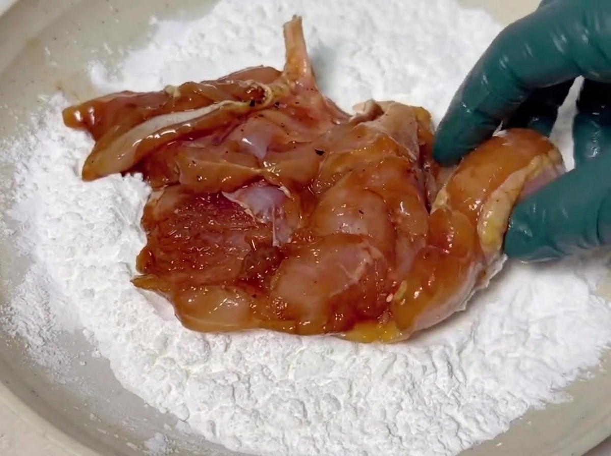 Trozos de pollo marinado siendo cubiertos con una capa blanca de maicena en un plato poco profundo.