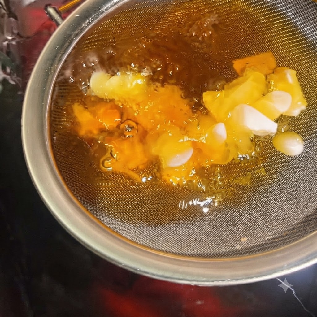 Rodajas de ajo volviéndose crujientes y doradas dentro de un colador sumergido en aceite caliente.