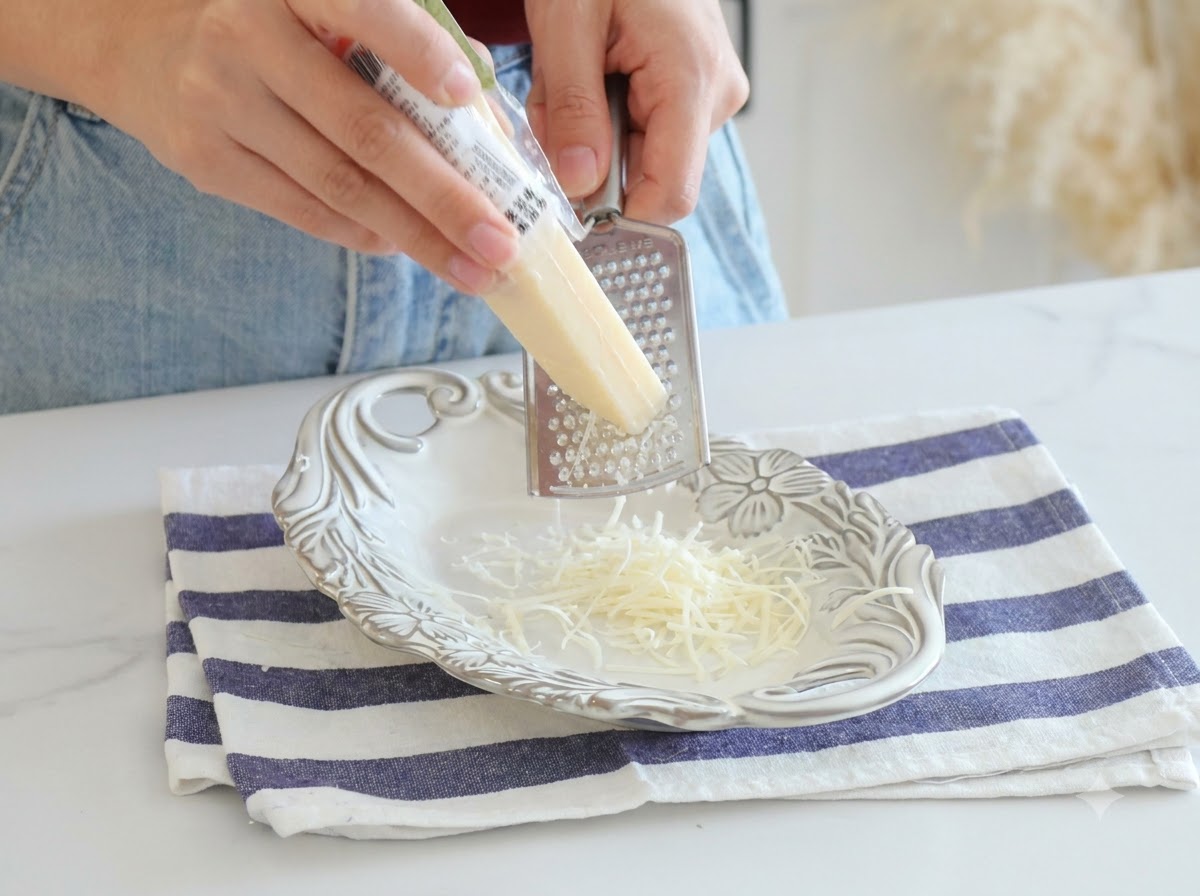 Queso parmesano siendo rallado fresco con un rallador de metal sobre un plato blanco.